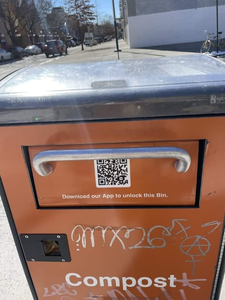 This meme is a photo of a public trash can with a sign that says "Download the app to unlock this bin." The image is likely meant to be humorous because it's absurd that a trash can would require a download to be used. The phrase "Download our App to unlock this bin" is likely a joke, implying that someone would need to download an app to use a simple trash can.